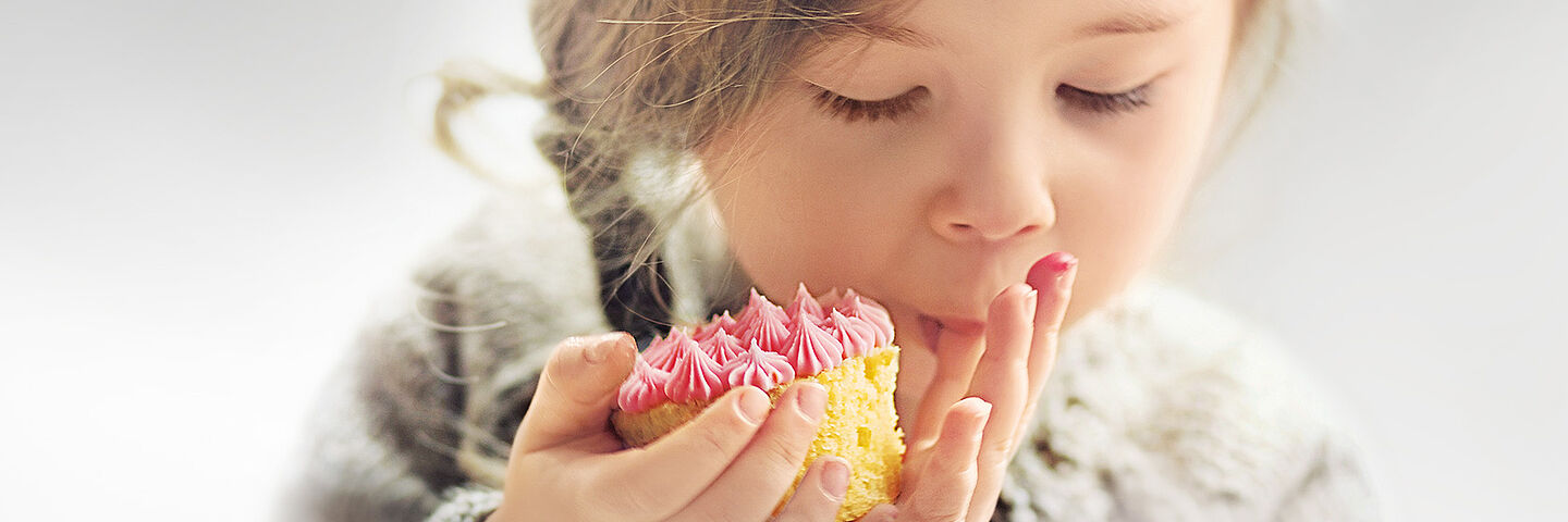 Kleines Mädchen isst einen Kuchen mit rosa Belag