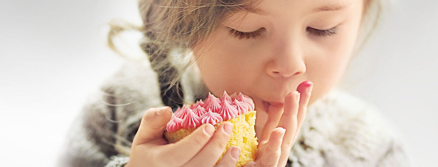 Kleines Mädchen isst einen Kuchen mit rosa Belag