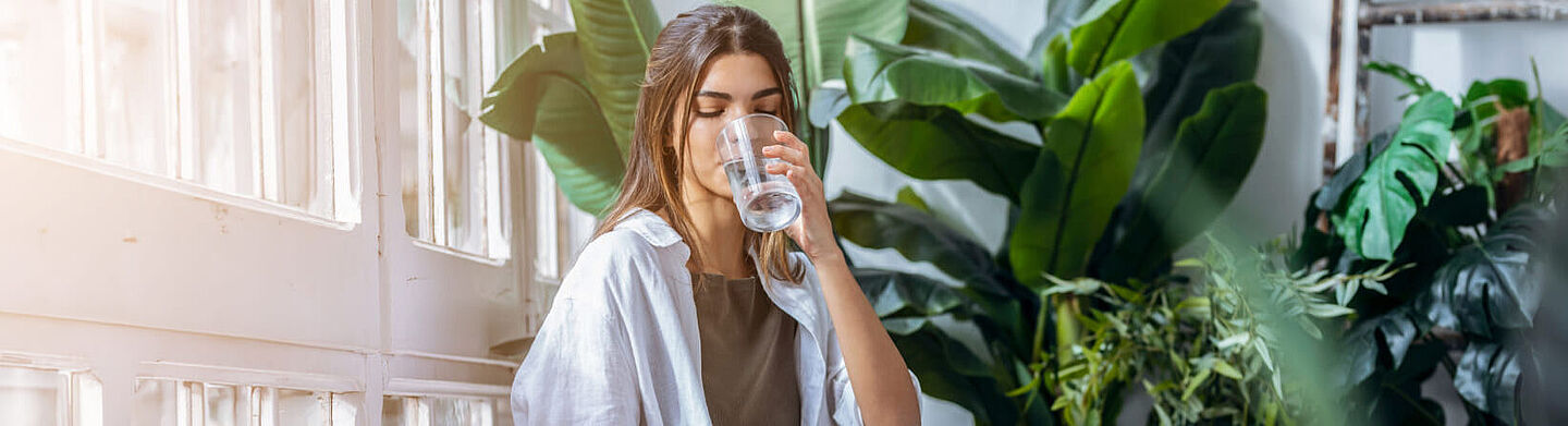 Chica bebiendo agua con hojas verdes en el fondo