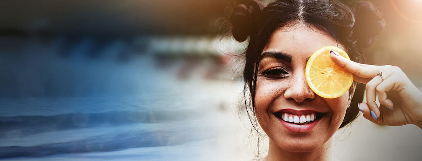 lachende Frau hält sich eine Zironenscheibe vor das linke Auge