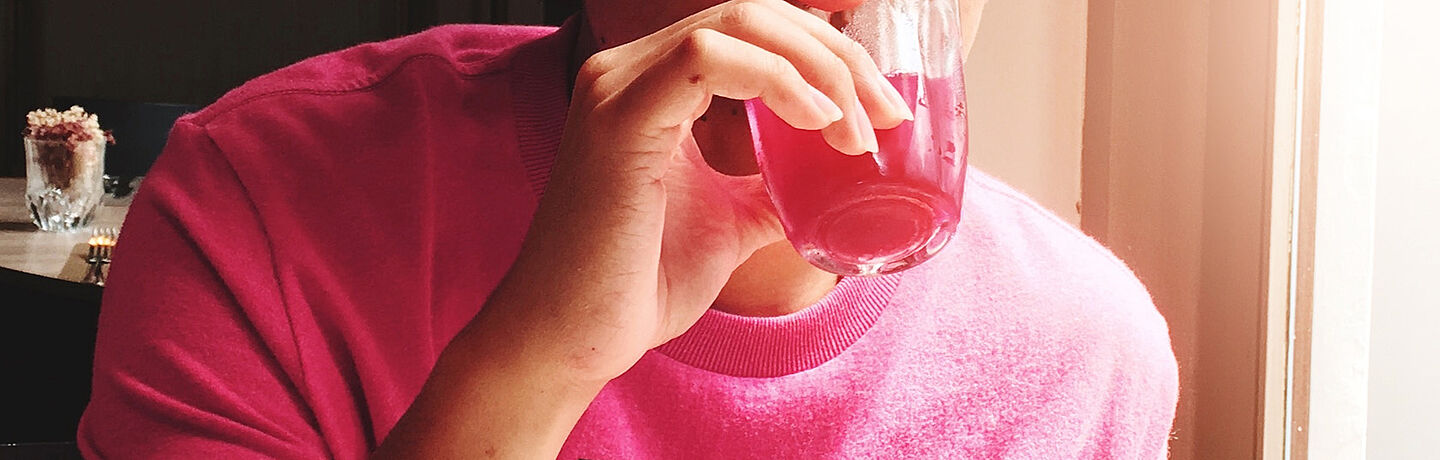 someone with pink shirt drinking a pink liquid