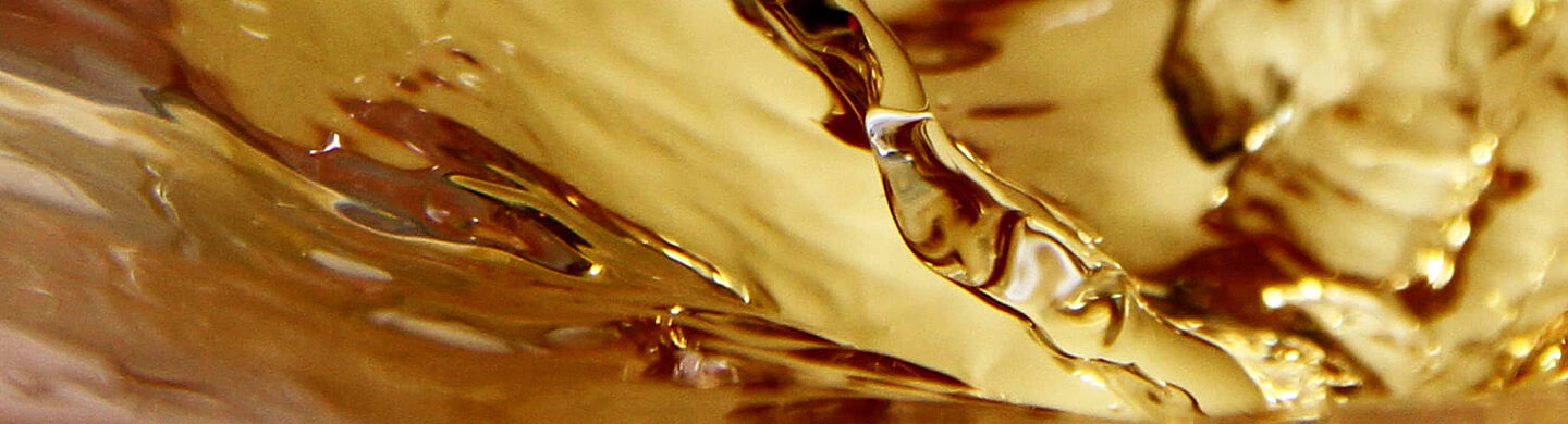 Nahaufnahme von goldenem Tee in Bewegung – fließende Wellen und glänzende Reflexionen.