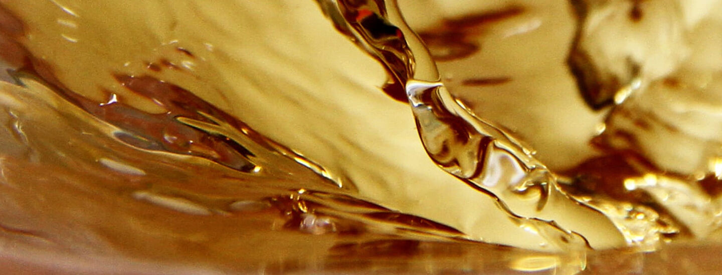 Nahaufnahme von goldenem Tee in Bewegung – fließende Wellen und glänzende Reflexionen.