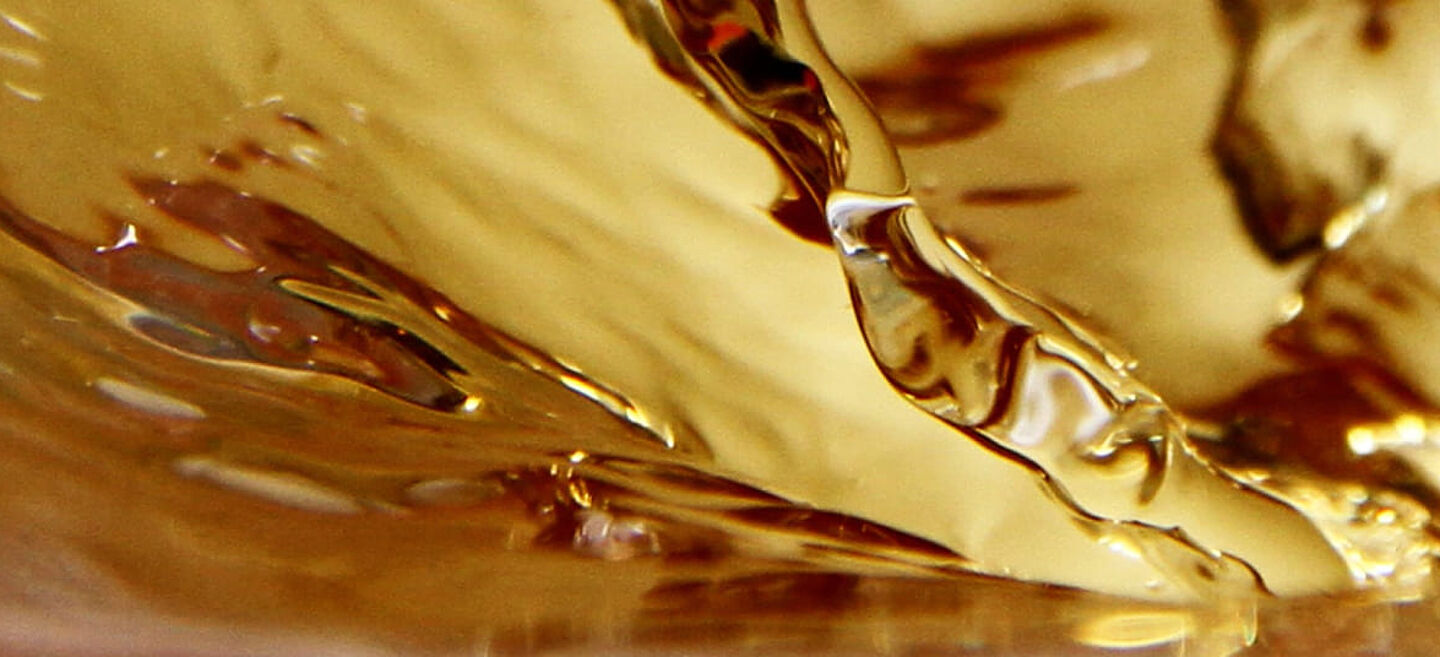 Nahaufnahme von goldenem Tee in Bewegung – fließende Wellen und glänzende Reflexionen.