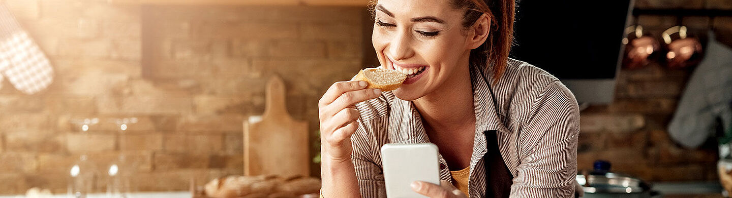 Frau am Handy, die Brot isst
