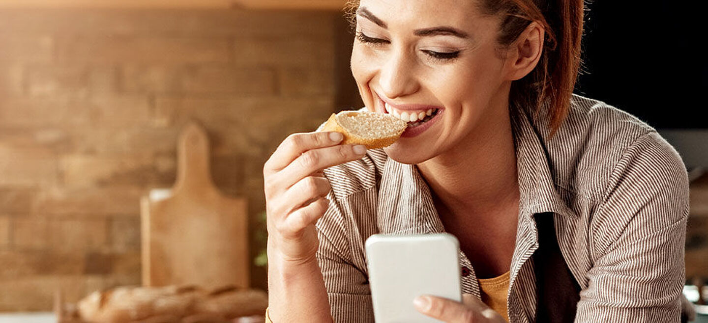 Frau am Handy, die Brot isst