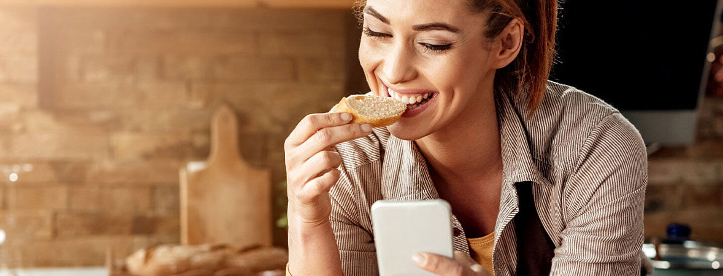 Frau am Handy, die Brot isst