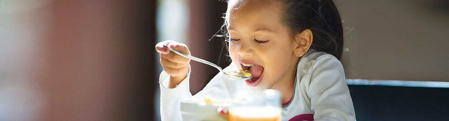 menina comendo cereais e um suco de laranja