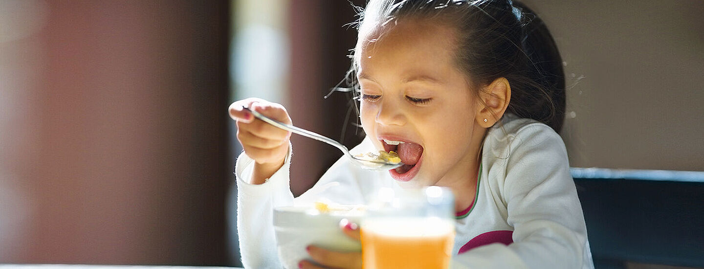 little kid eating a bowl of cereals with an orange juice 