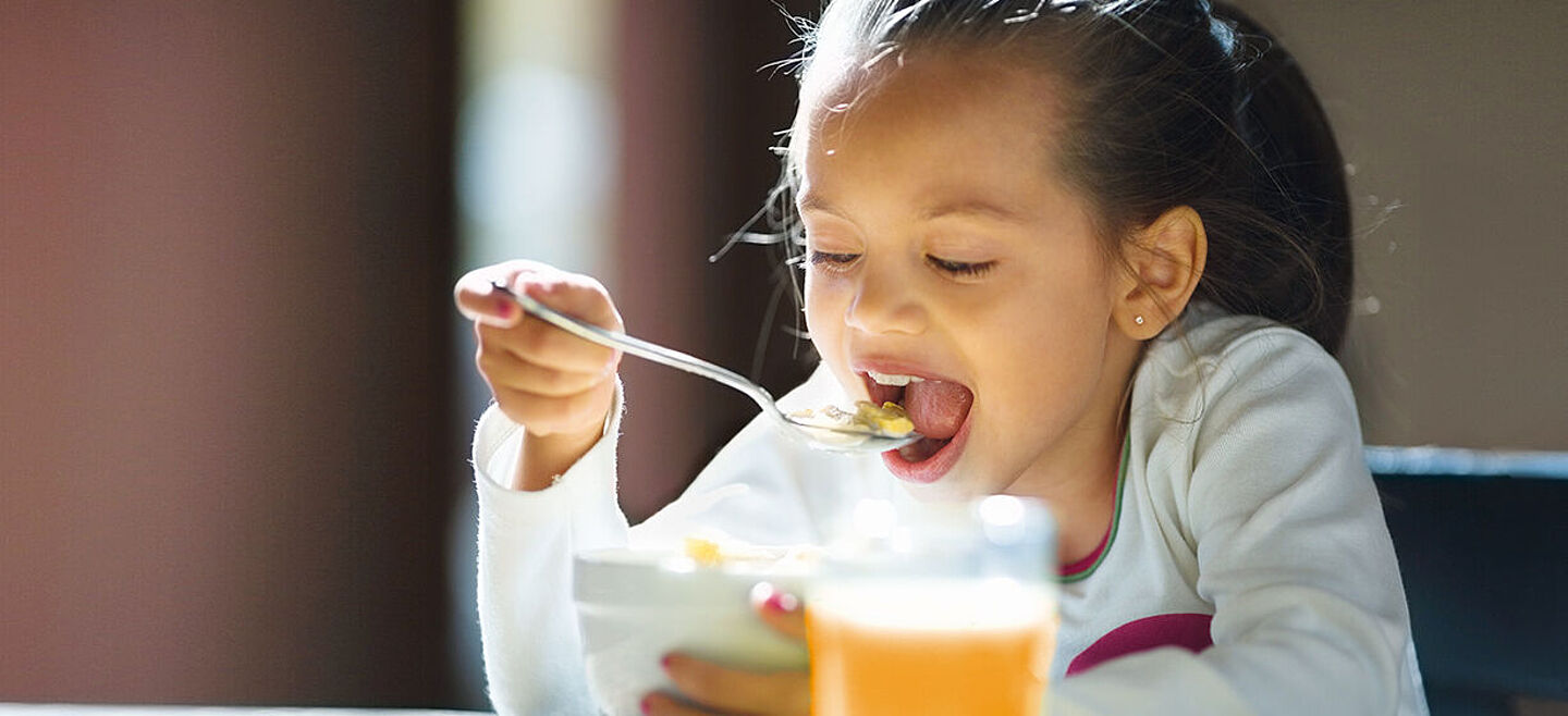 menina comendo cereais e um suco de laranja