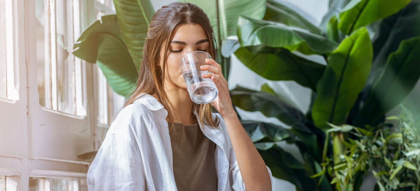 Chica bebiendo agua con hojas verdes en el fondo