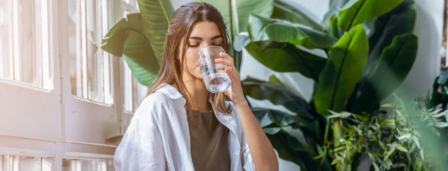 Chica bebiendo agua con hojas verdes en el fondo