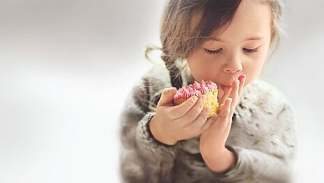 Uma menina está comendo um cupcake rosa