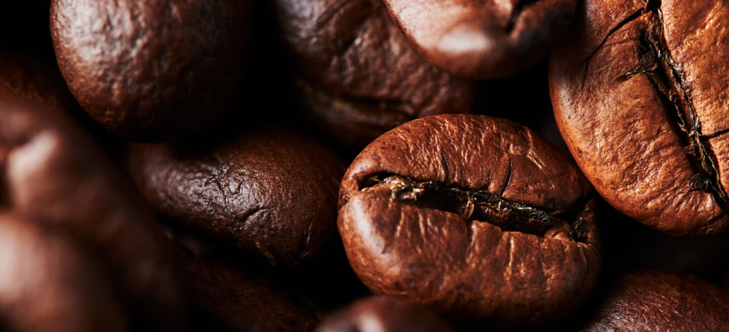 Kavrulmuş kahve çekirdeklerinin makro çekimi – koyu kahverengi çekirdekler, kavrulma izleri ve dokusu görünür.