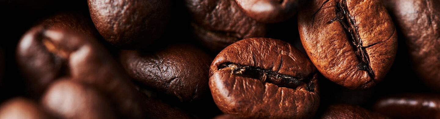 Kavrulmuş kahve çekirdeklerinin makro çekimi – koyu kahverengi çekirdekler, kavrulma izleri ve dokusu görünür.