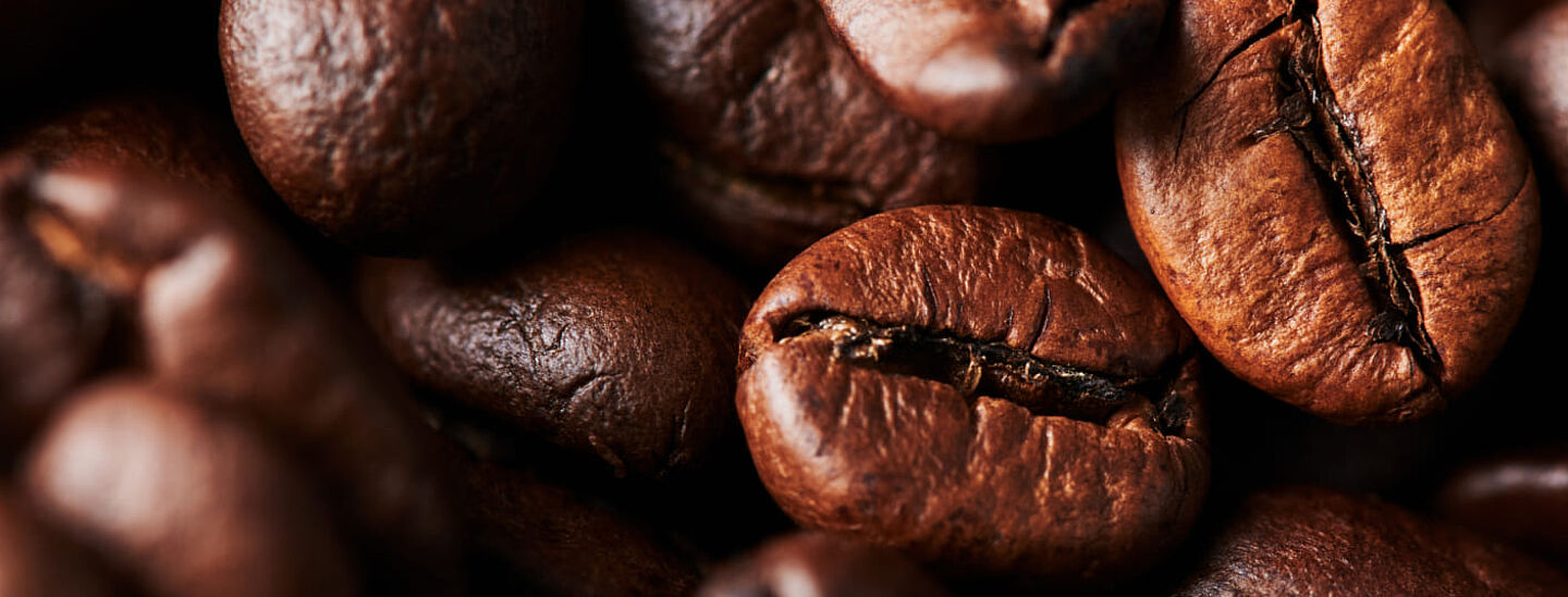 Kavrulmuş kahve çekirdeklerinin makro çekimi – koyu kahverengi çekirdekler, kavrulma izleri ve dokusu görünür.